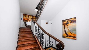 Una escalera con barandilla de madera y balaustres de metal negro, que lleva a un rellano con un cuadro abstracto de colores.