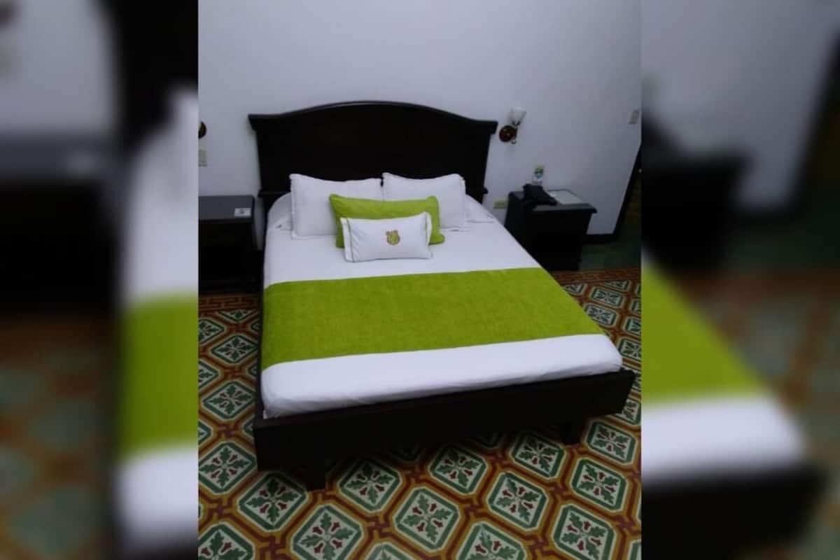 A neatly made bed with a green and white bedspread, a black headboard, and a patterned floor.