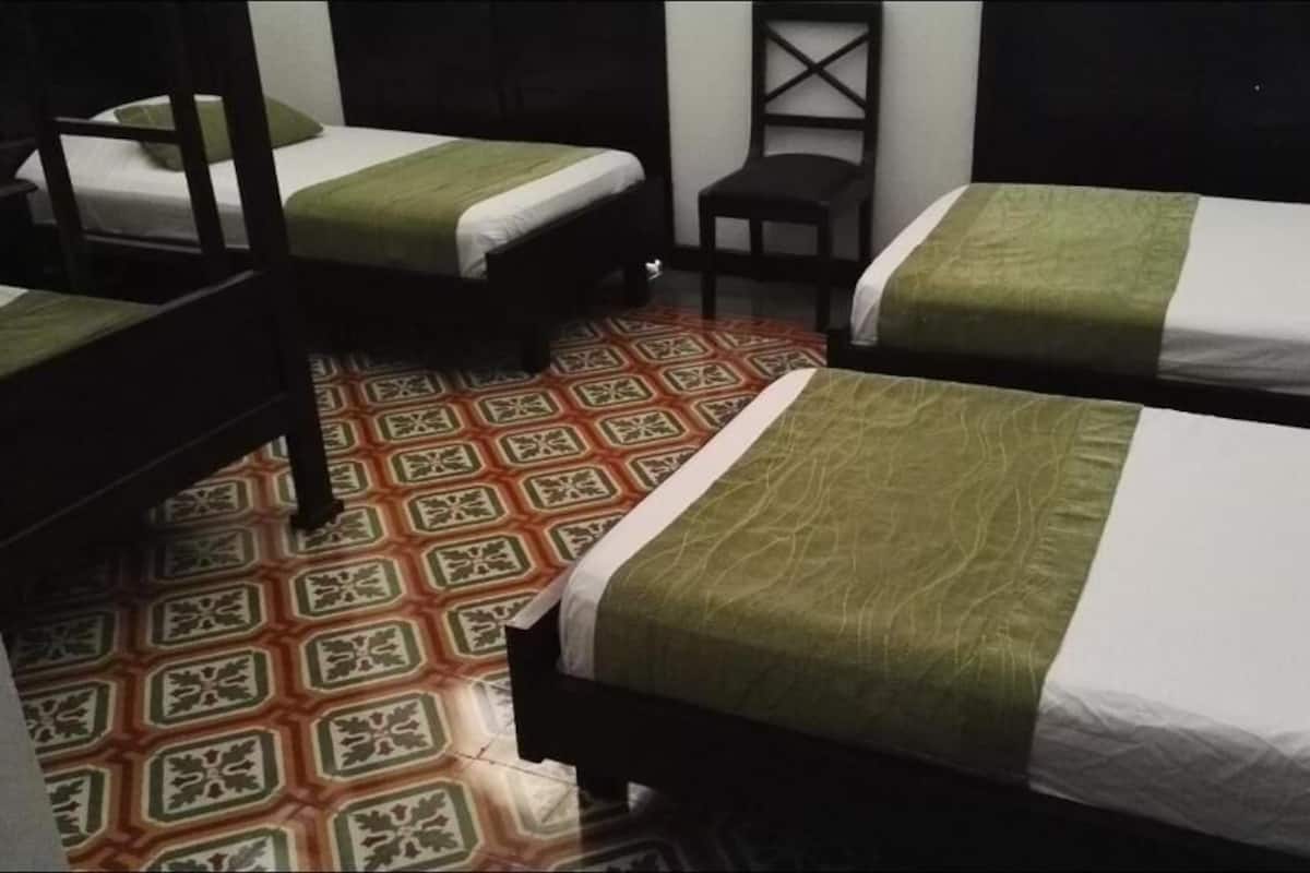 A room with four single beds, each with a green and white bedspread. The floor has a patterned tile design.