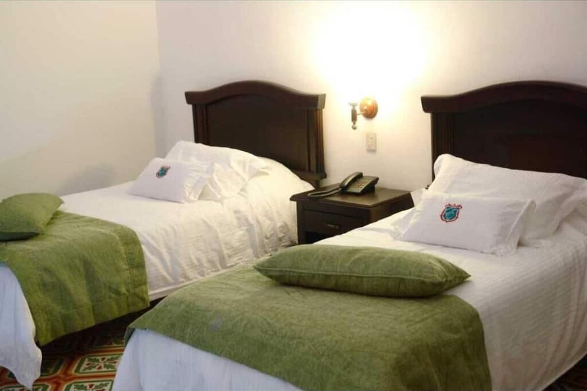 Two single beds with green headboards, white bedding, and matching pillows. Each bed has a bedside table with a lamp and a phone.