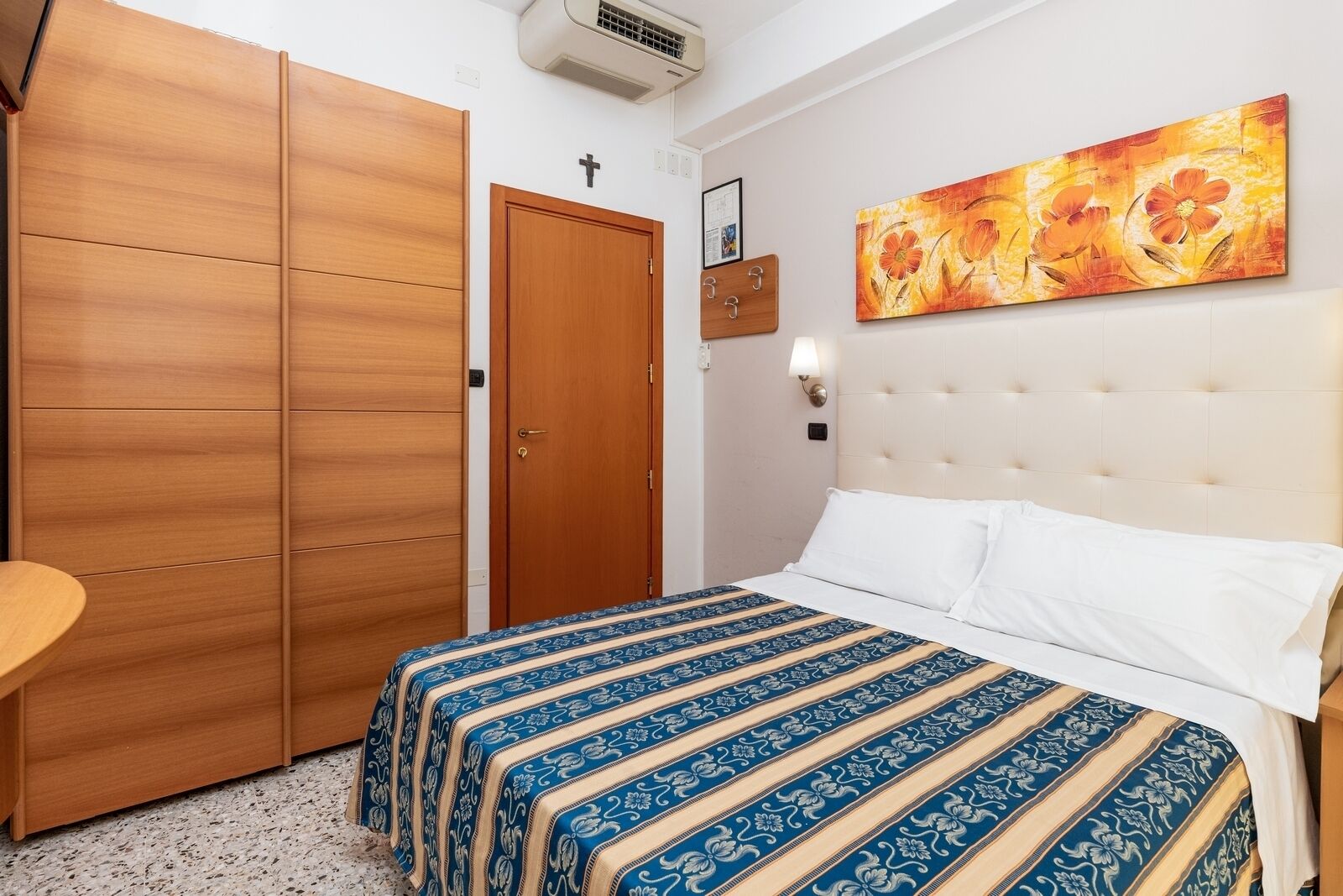Una camera da letto con un letto, un armadio in legno, una porta con una croce, una lampada a parete e un quadro.