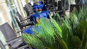Zona salotto all'aperto con tavoli ricoperti da tovaglie blu, circondata da sedie nere.