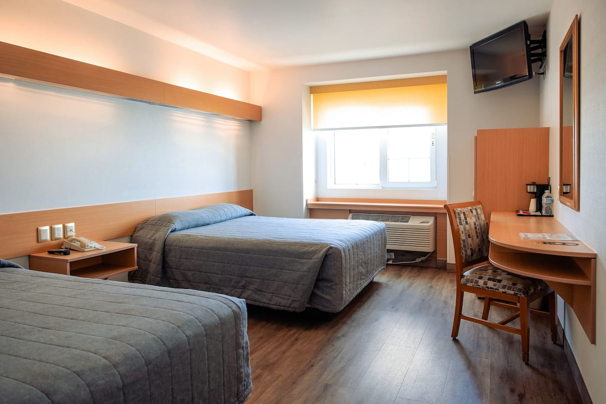 A hotel room with two beds, a desk, a chair, a TV, and a window.