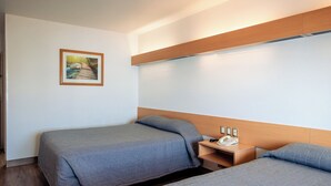 Habitación de hotel con dos camas, cabecero de madera, mesita de noche con teléfono y un cuadro en la pared.