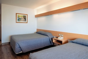 Habitación de hotel con dos camas, cabecero de madera, mesita de noche con teléfono y un cuadro en la pared.