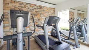 Un gimnasio con cintas de correr y una máquina elíptica, pared de piedra y un espejo grande.