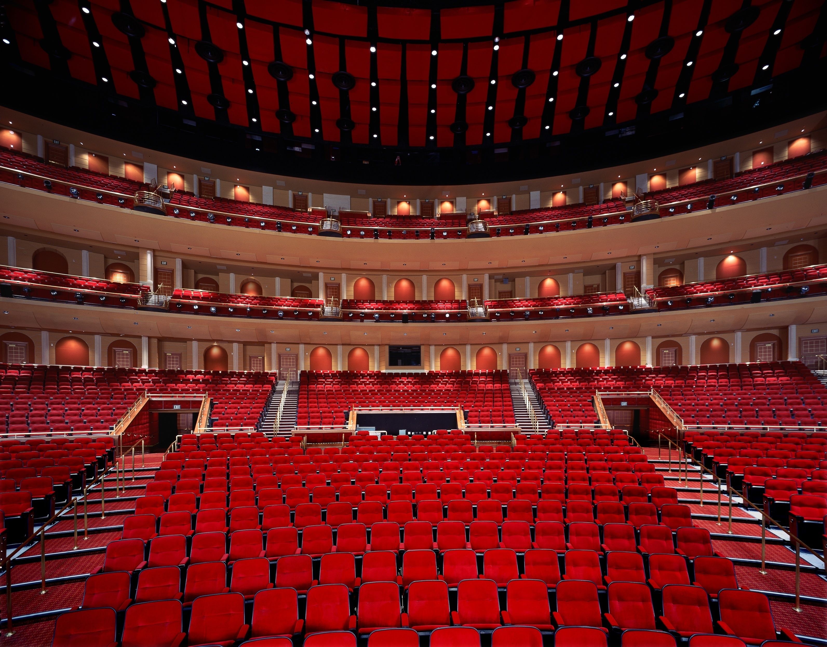 Un auditorio de varios niveles con asientos rojos y un escenario central.