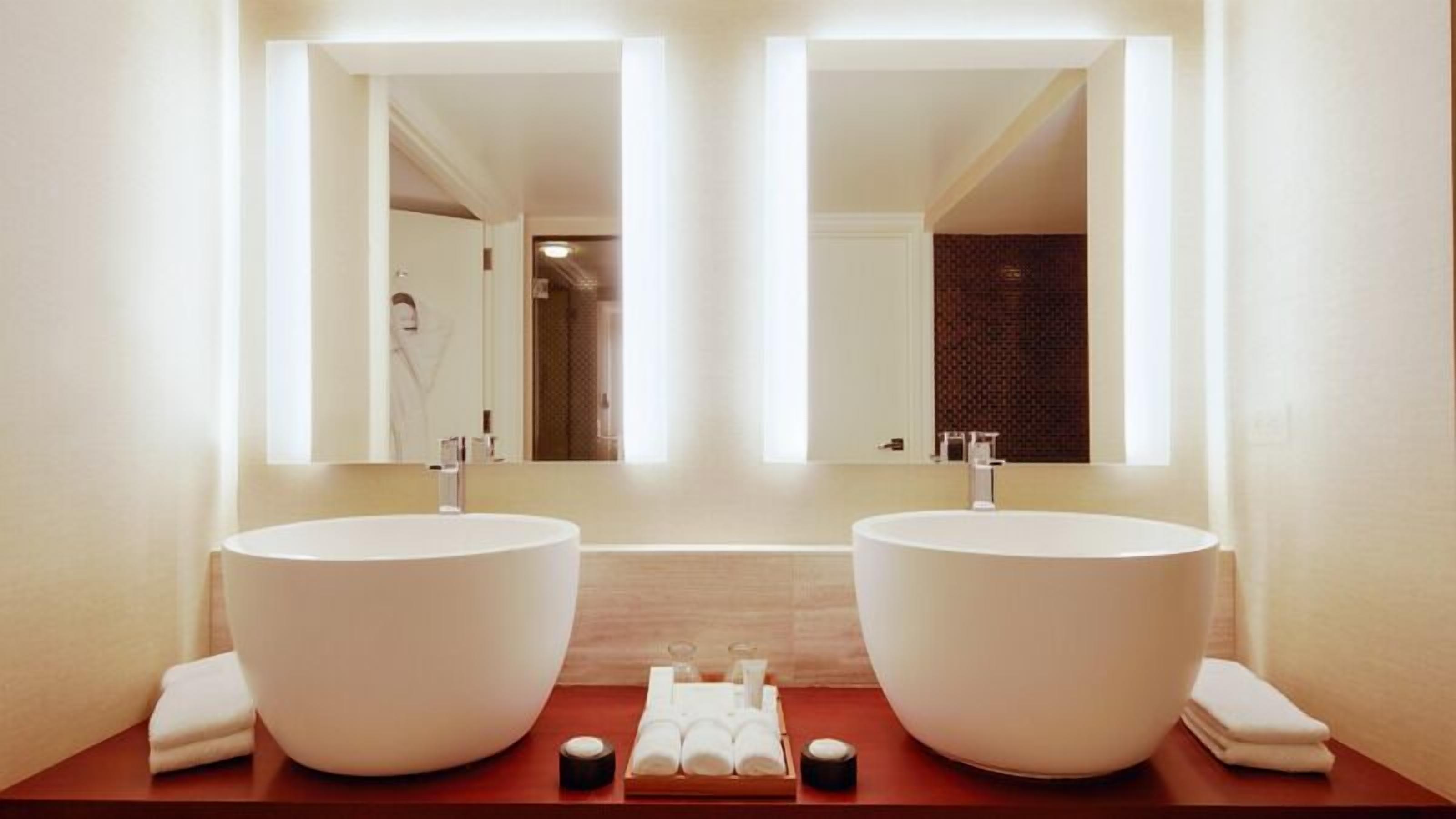 Une salle de bain avec deux grands lavabos blancs, un miroir et un meuble-lavabo en bois.
