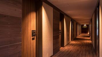 Un largo y estrecho pasillo con paredes y puertas de madera, con el número 306, que conduce a una habitación luminosa al final.