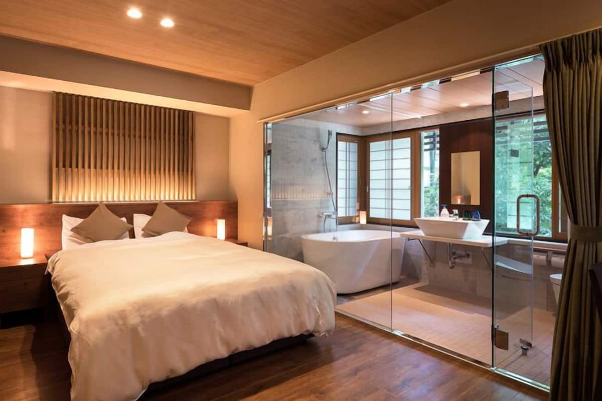 A modern bedroom with a large bed, a separate bathroom with a bathtub, and a glass-enclosed shower area.