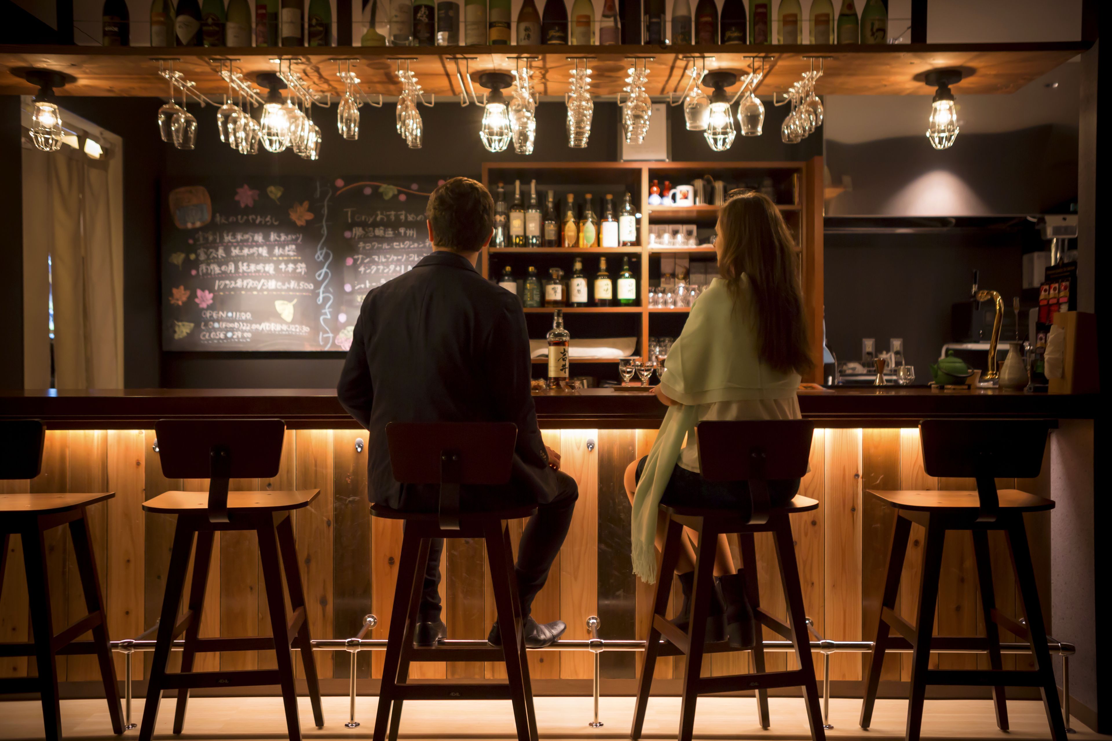 A bar area with wooden stools, a bar counter, and hanging light fixtures.