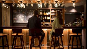 A bar area with wooden stools, a bar counter, and hanging light fixtures.
