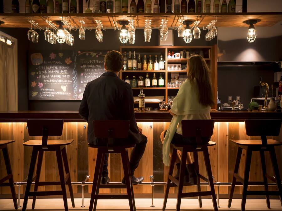 A bar area with wooden stools, a bar counter, and hanging light fixtures.