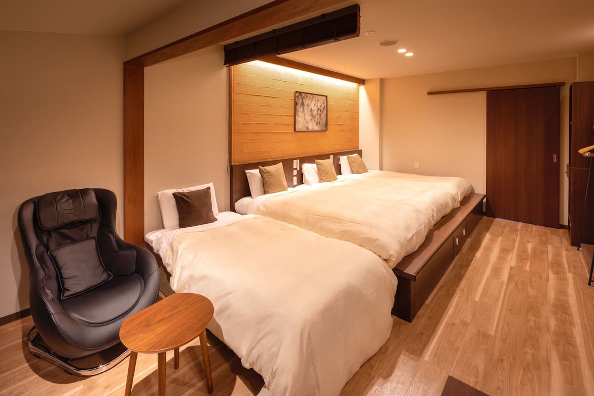 A hotel room with two beds, a massage chair, a small wooden table, and a wooden headboard.