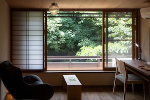 A room with a large window, a desk, a chair, and a small table.