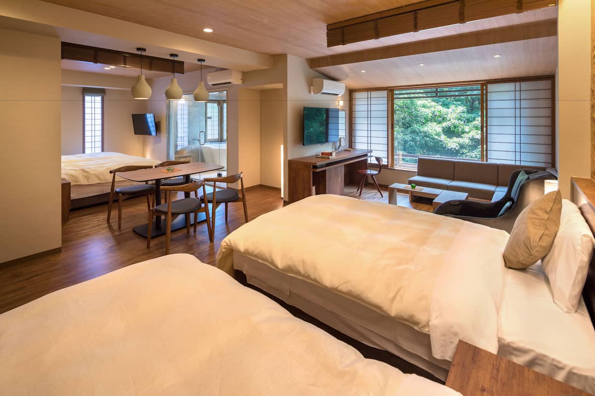 A modern hotel room with a large bed, a desk, and a seating area with a view of greenery.