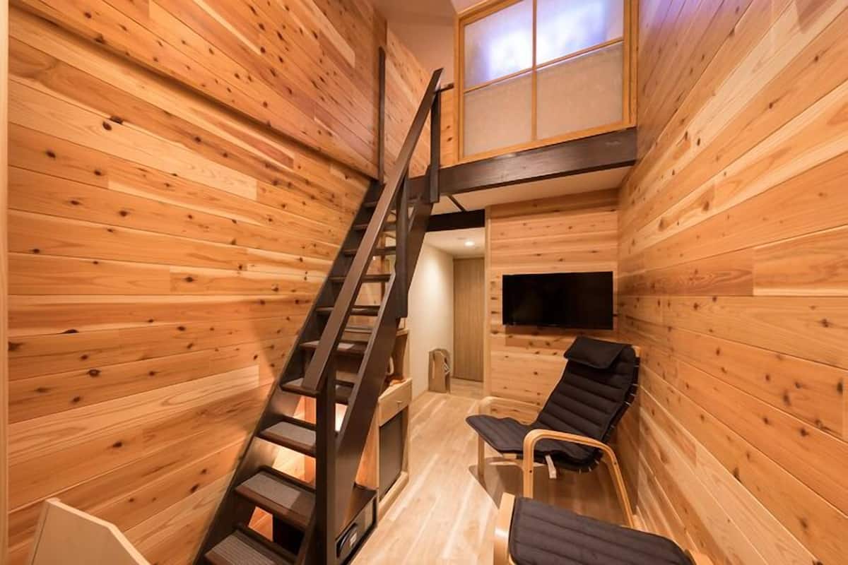 A wooden interior with a staircase, a flat-screen TV, and two reclining chairs.