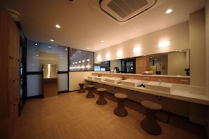 A modern bathroom with multiple sinks, a large mirror, and wooden stools.