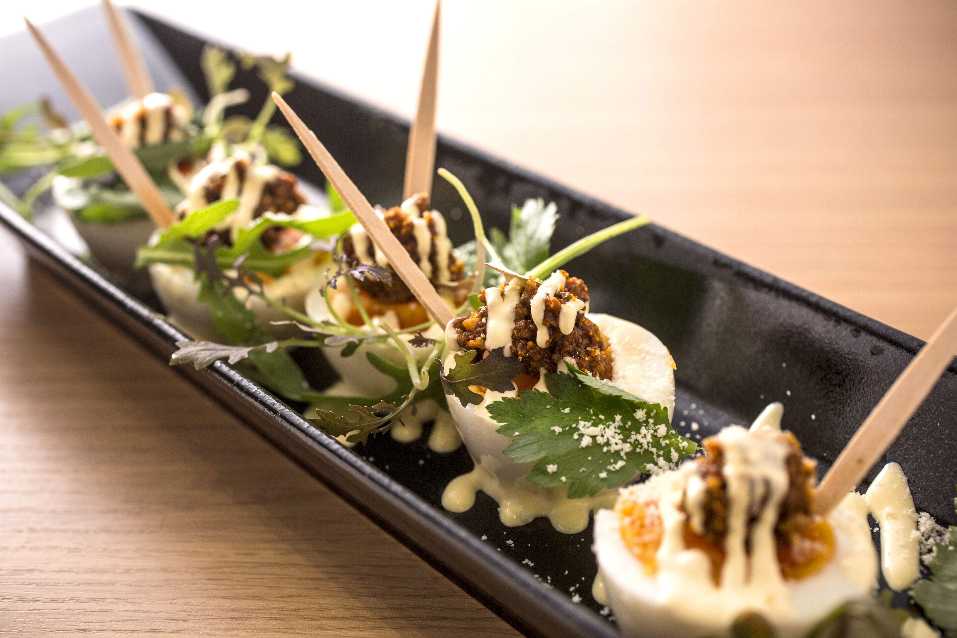 A black rectangular plate with food items, including a dessert with a white topping and a sauce, garnished with green leaves and a sprinkle of white powder.
