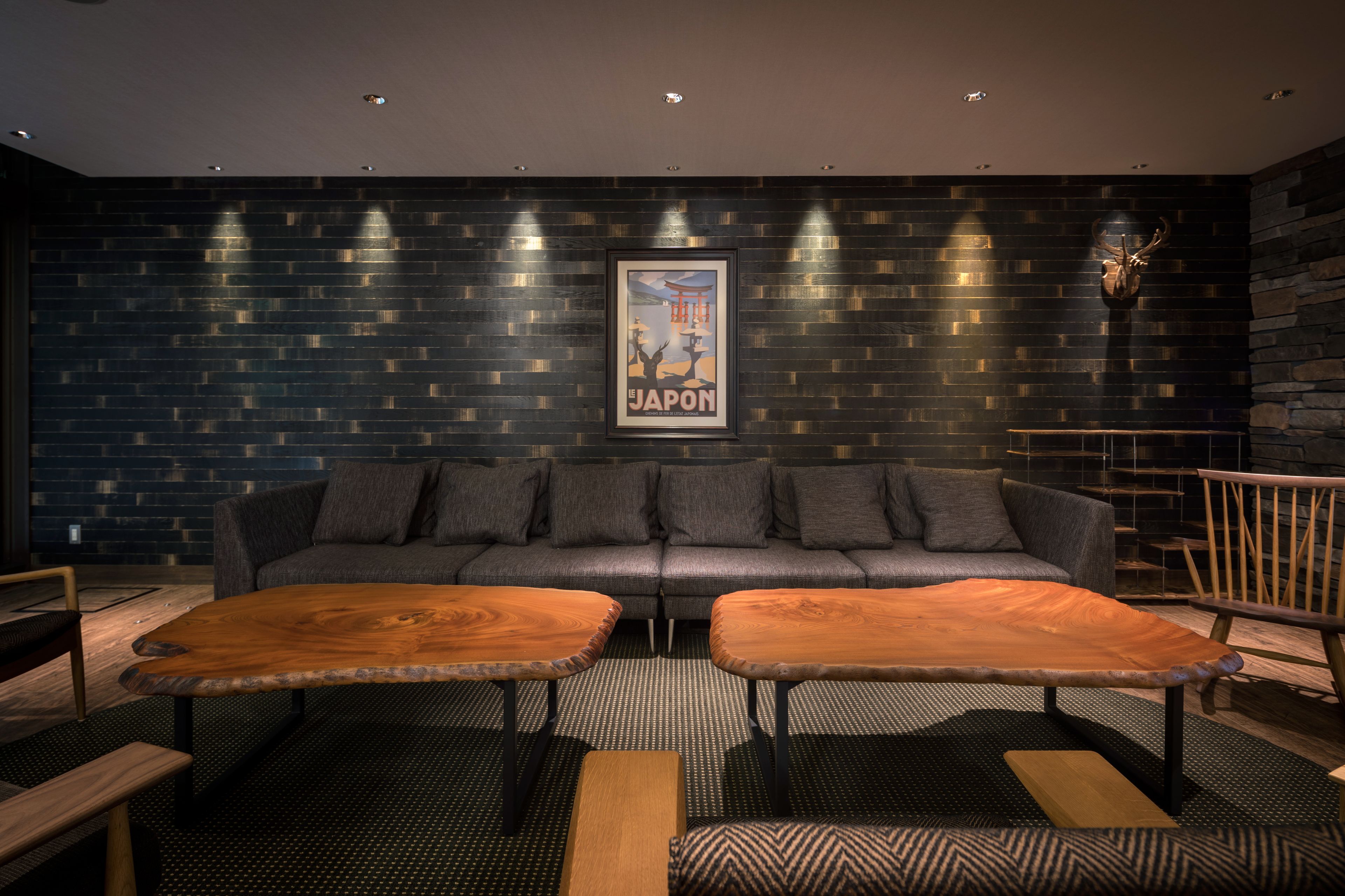 A modern lounge area with a dark brick wall, a sofa, two wooden tables, and a framed picture of Japan.