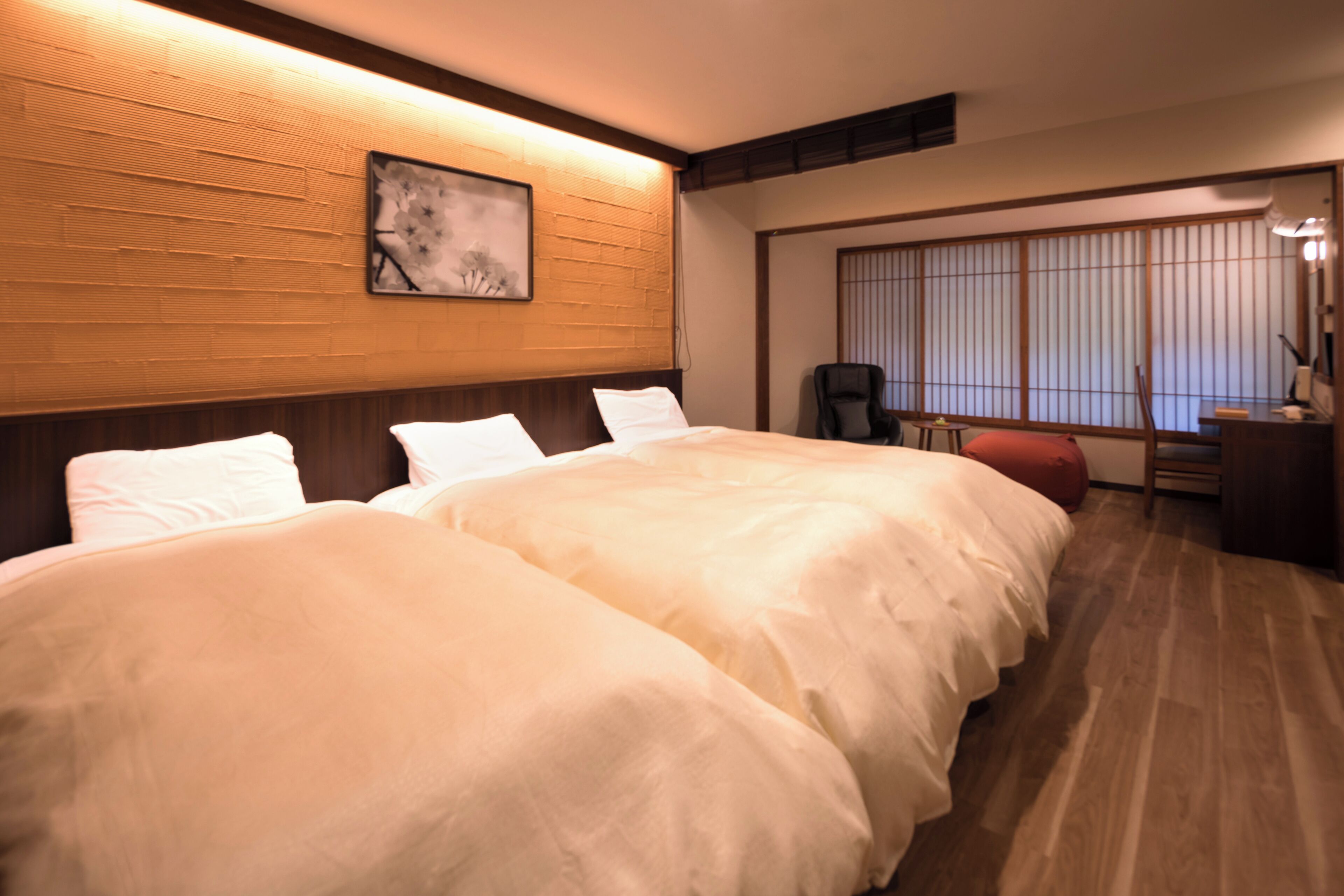 A hotel room with two beds, a desk, a chair, and a large window with blinds.