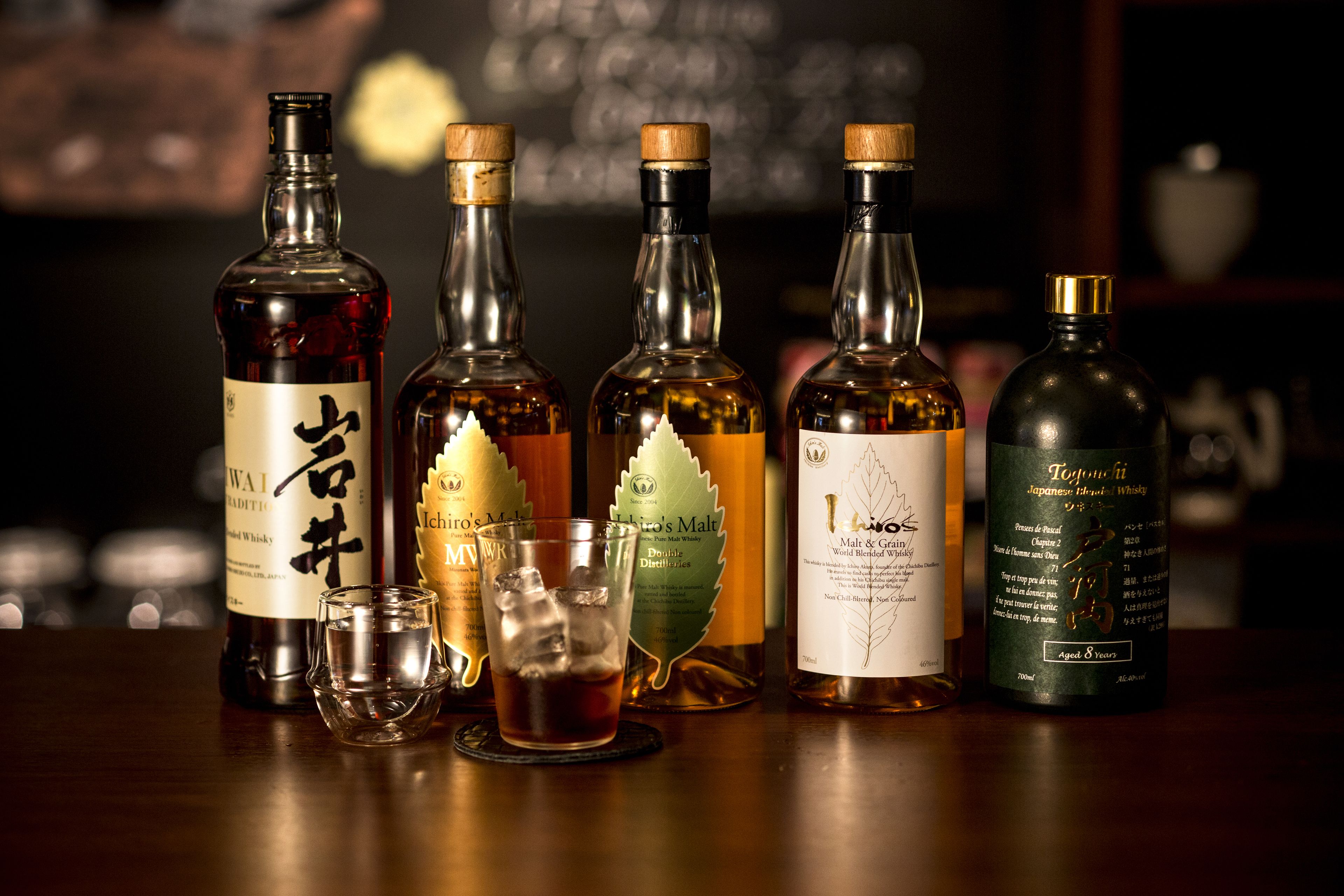 Variedad de botellas de whisky y vasos sobre una barra.