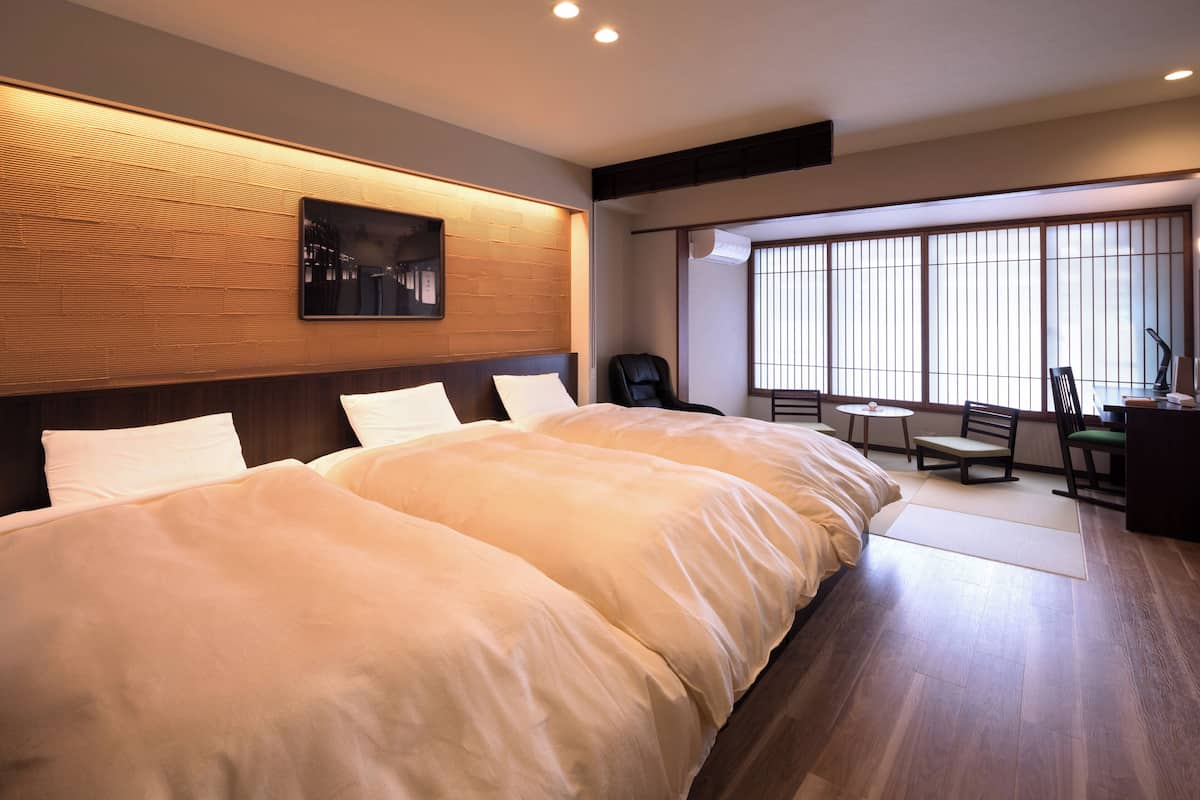A hotel room with a large bed, a small table, a chair, and a desk with a lamp.