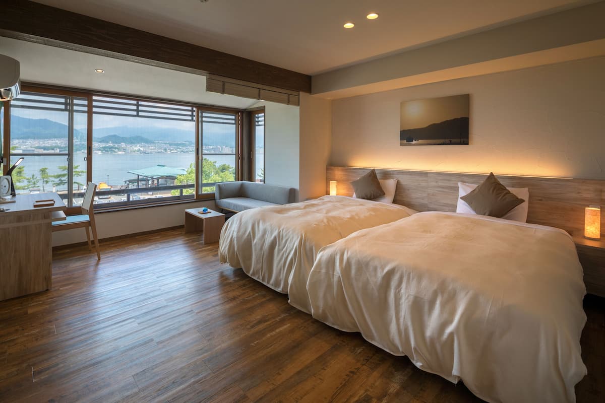 A modern hotel room with a large bed, a desk, and a view of a city and water.