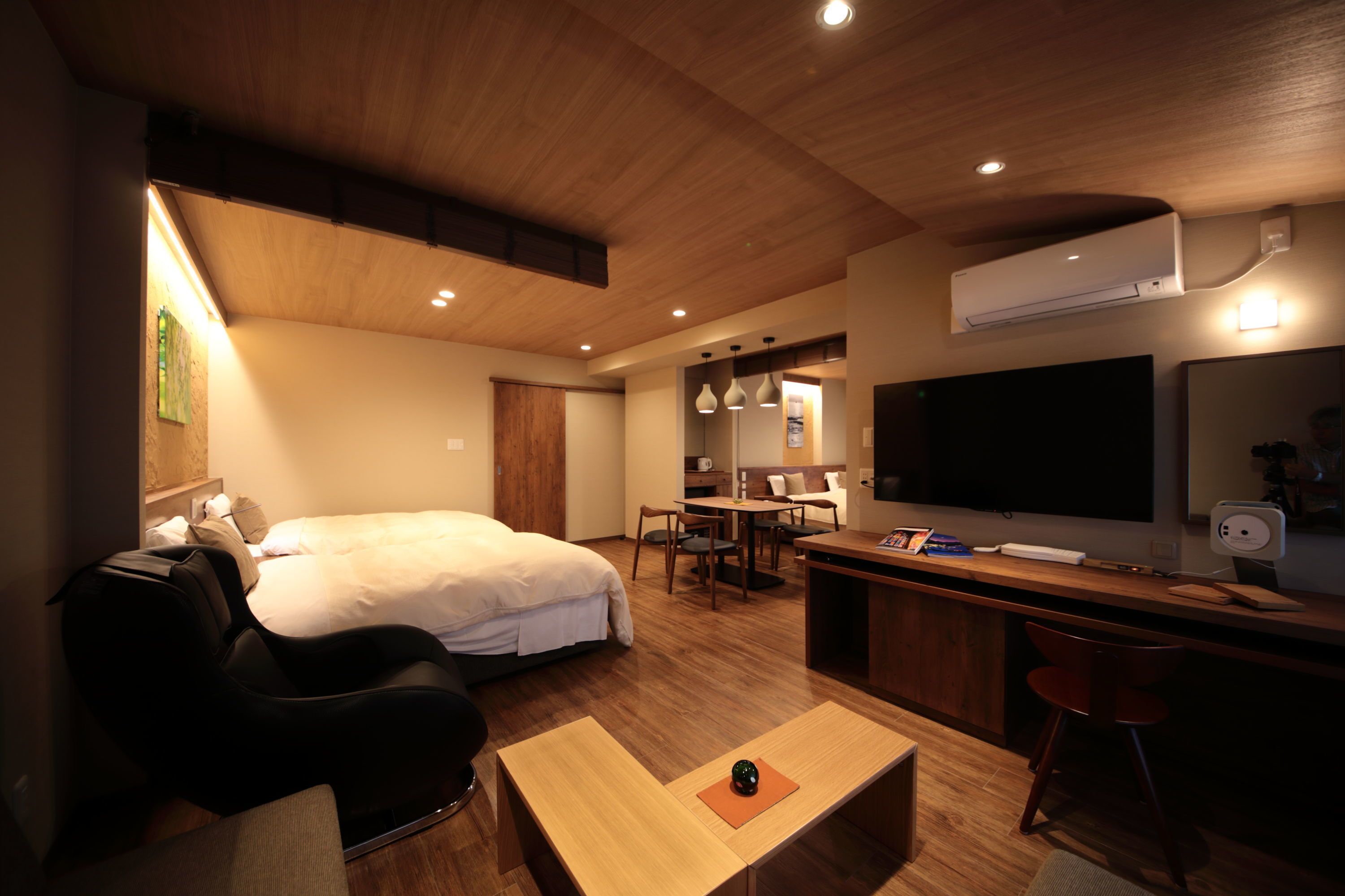 Una habitación de hotel moderna con una cama, una silla de masajes, un comedor y un televisor.