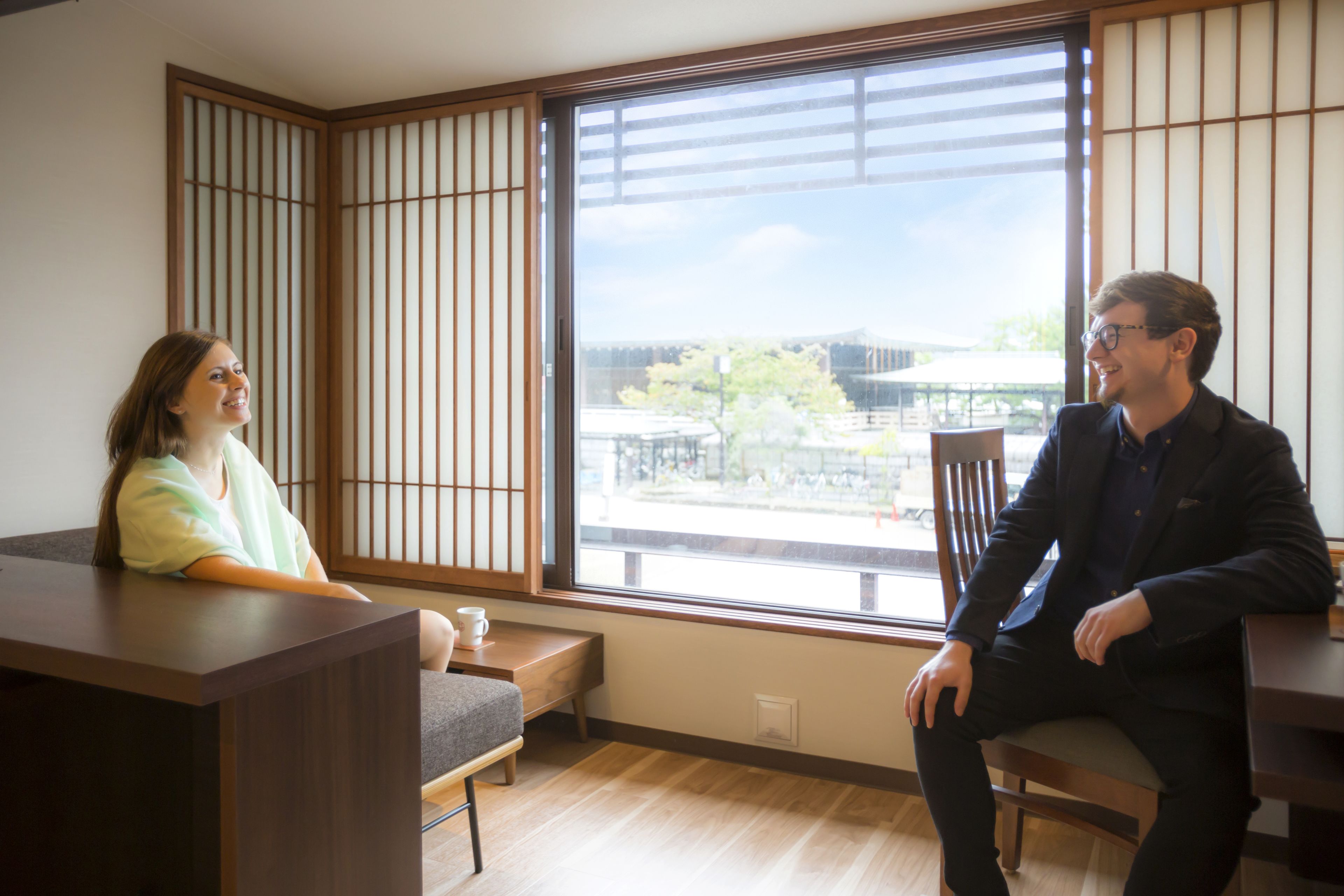 A room with a large window, a wooden floor, and a low table.