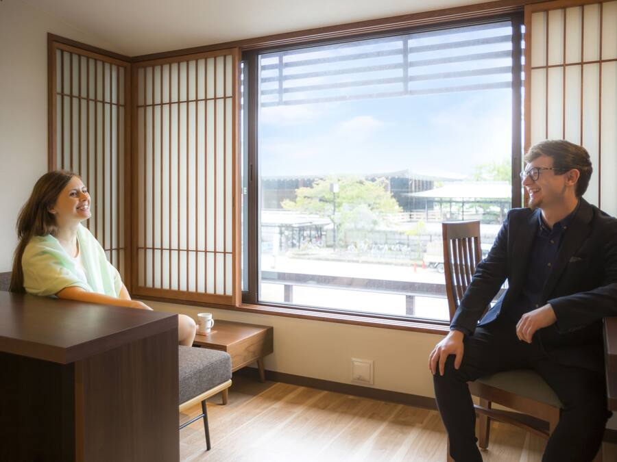 A room with a large window, a wooden floor, and a low table.