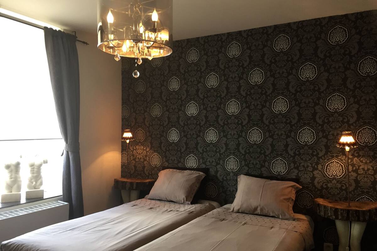 A double bed with a patterned headboard, two bedside tables with lamps, and a chandelier.
