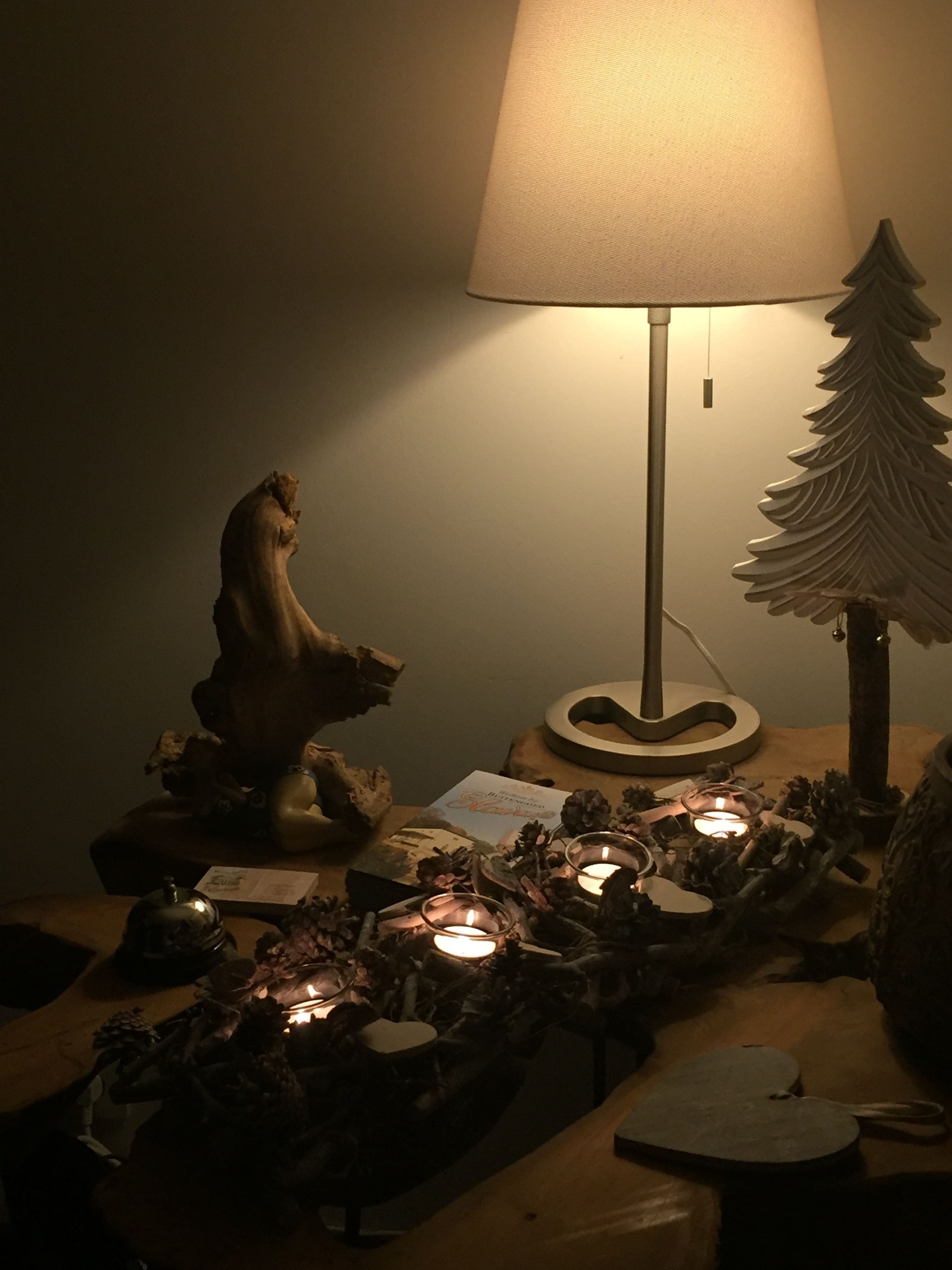 Una mesa con una lámpara decorativa, un pequeño árbol de Navidad y velas.