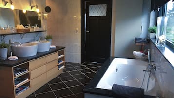 A modern bathroom with two sinks, a large bathtub, and a window providing natural light.