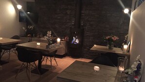 Un restaurante tenuemente iluminado con paredes de piedra, mesas con velas y una chimenea.
