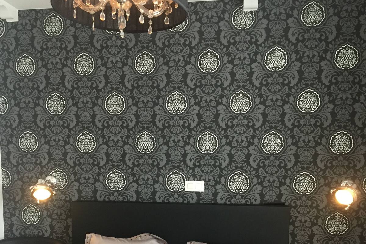 A bedroom with a large bed, two pillows, a chandelier, and patterned wallpaper.