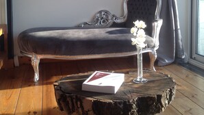 Una habitación con un sofá de terciopelo oscuro, un espejo decorativo y una mesa de centro de madera rústica con un libro y flores.
