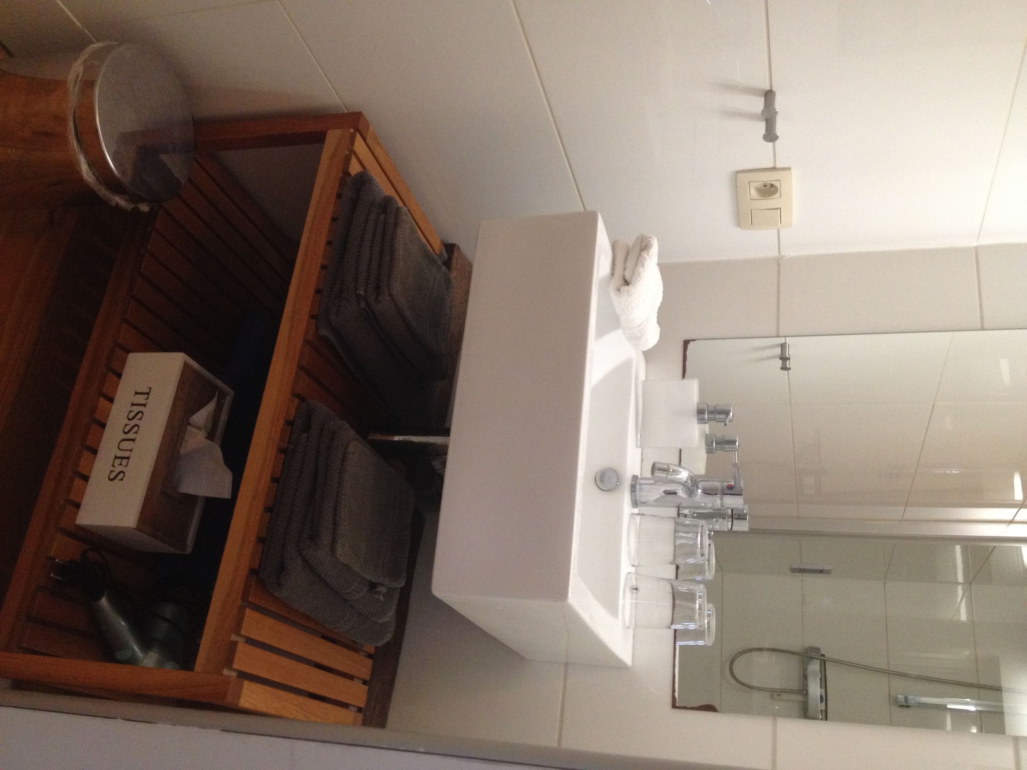A bathroom with a wooden shelf holding towels and a box labeled "TISSUES".