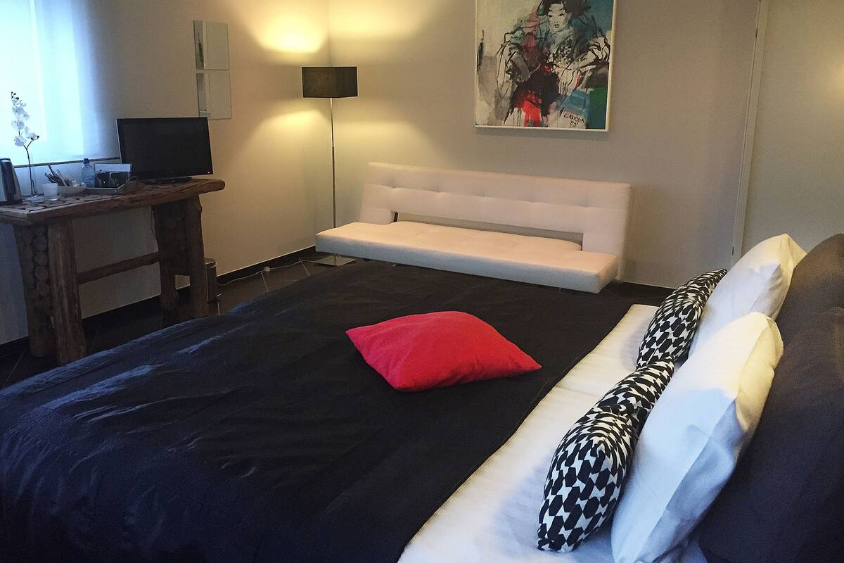 A bedroom with a bed, a desk, a chair, a sofa, and a painting on the wall.