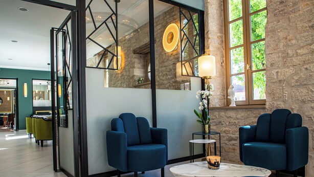 A modern interior with two blue armchairs, a marble coffee table, and a stone wall. - Olivier leflaive (Puligny-Montrachet)