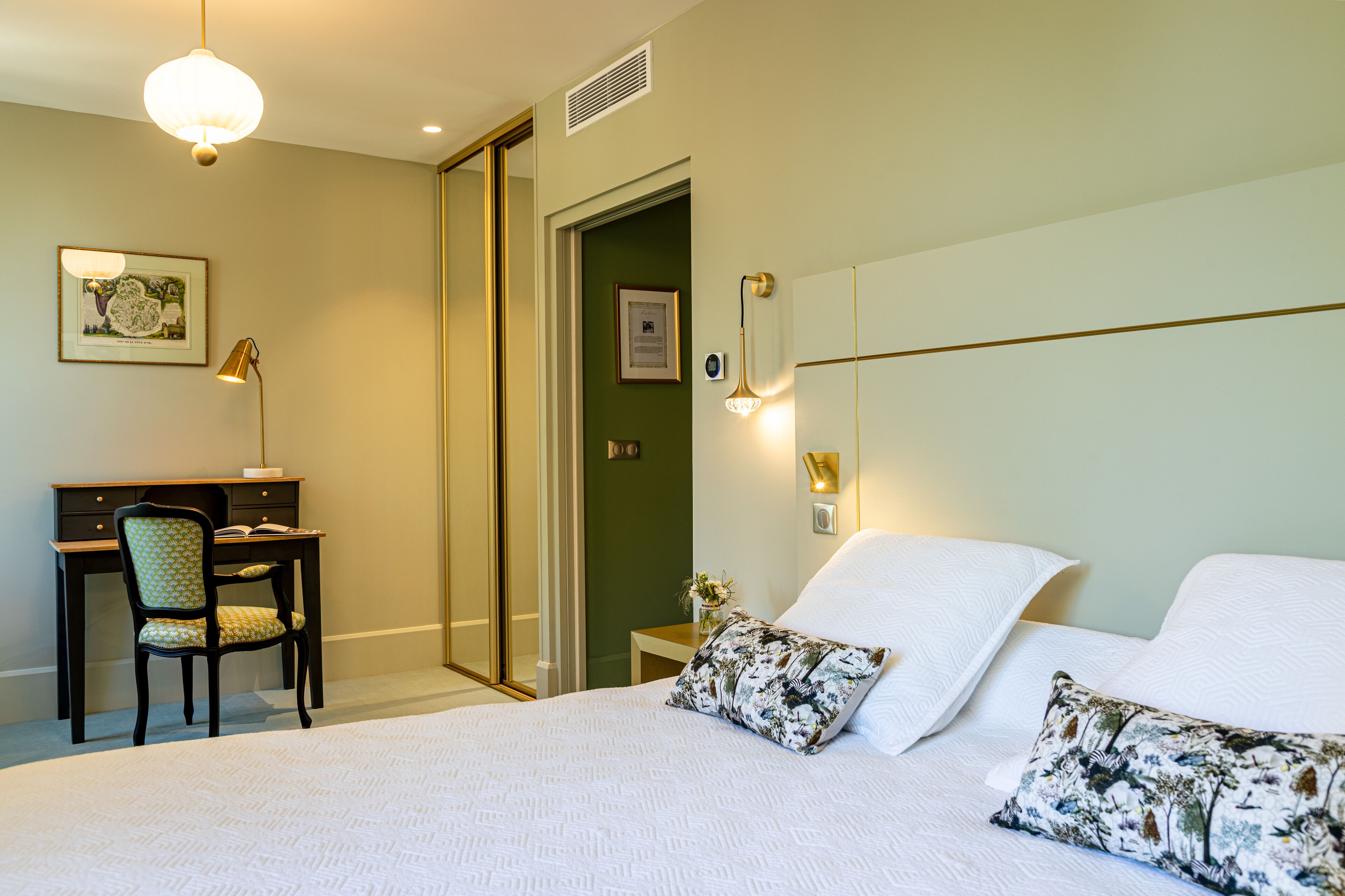 Ein Schlafzimmer mit einem Bett, zwei Kissen, einem Schreibtisch mit Stuhl, einem gerahmten Bild und einer Wandleuchte.