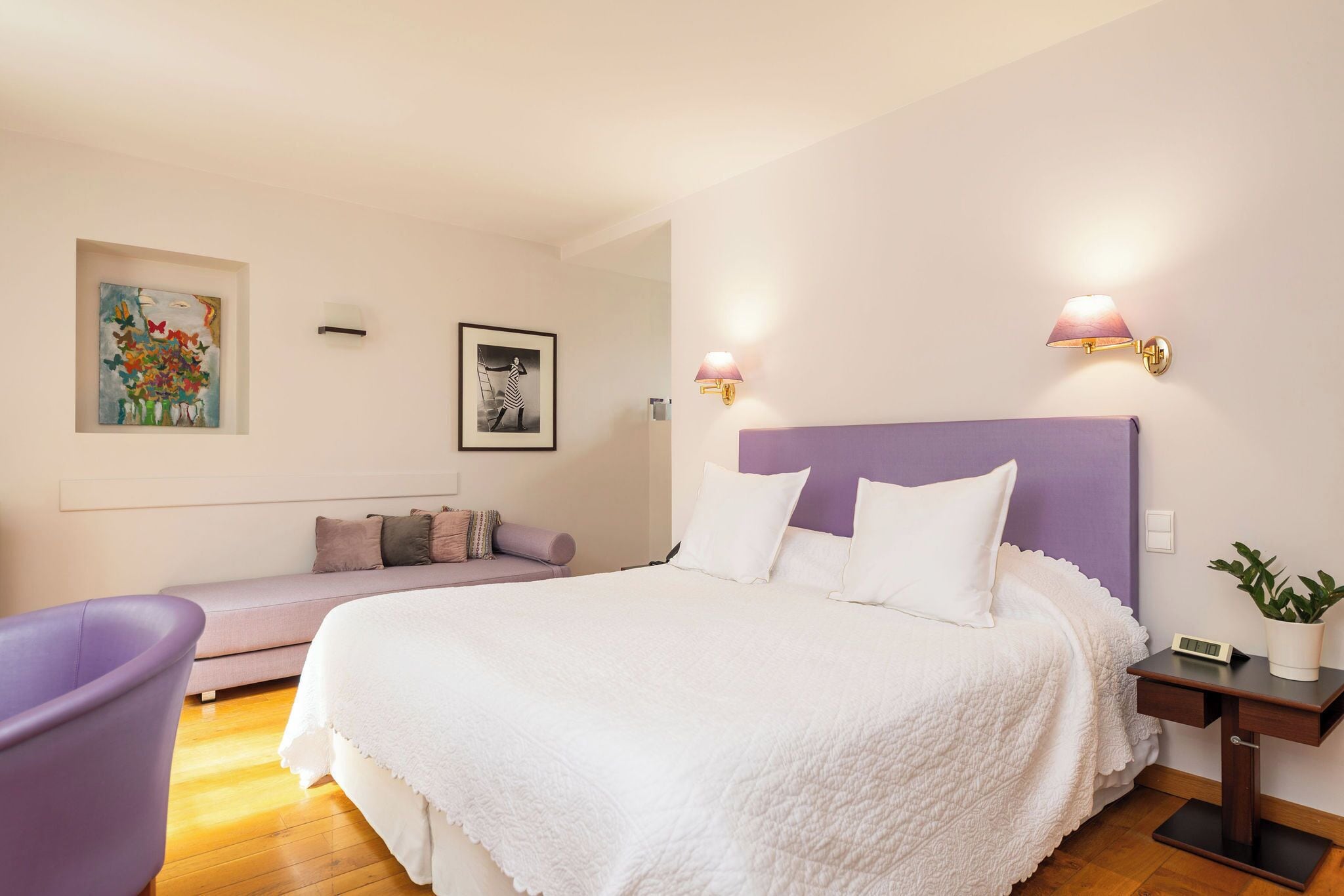 Une chambre à coucher comprenant un lit, une table de chevet, une lampe, une horloge murale, un tableau et un banc.