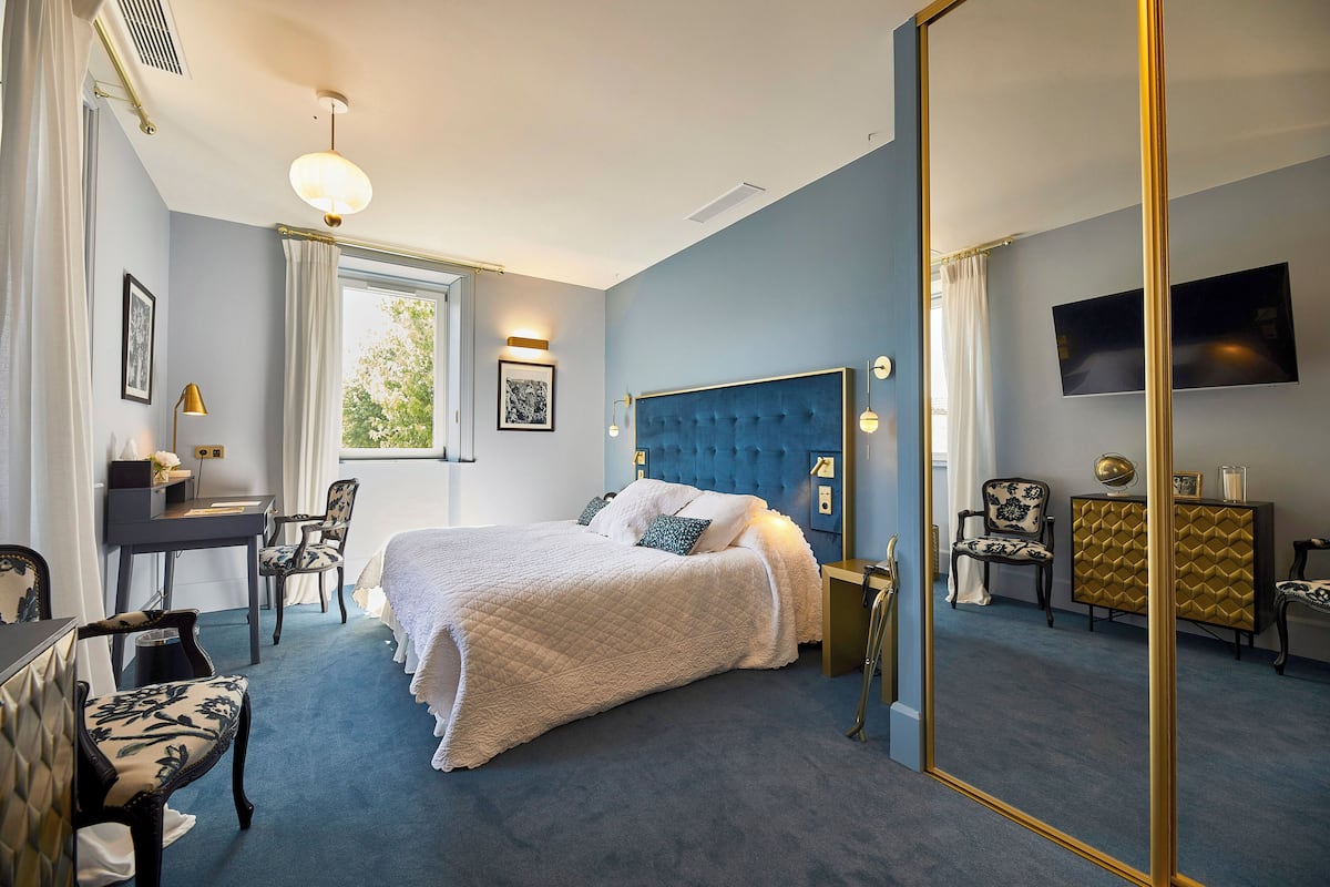 Ein Hotelzimmer mit einem großen Bett, einem Schreibtisch, einem Sessel, einem Fernseher und einem Spiegel.
