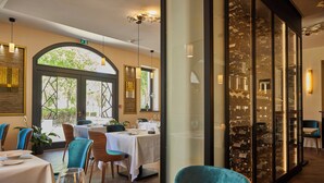 A restaurant with tables set for dining, a wine rack, and a view of the outdoors. - Olivier leflaive (Puligny-Montrachet)