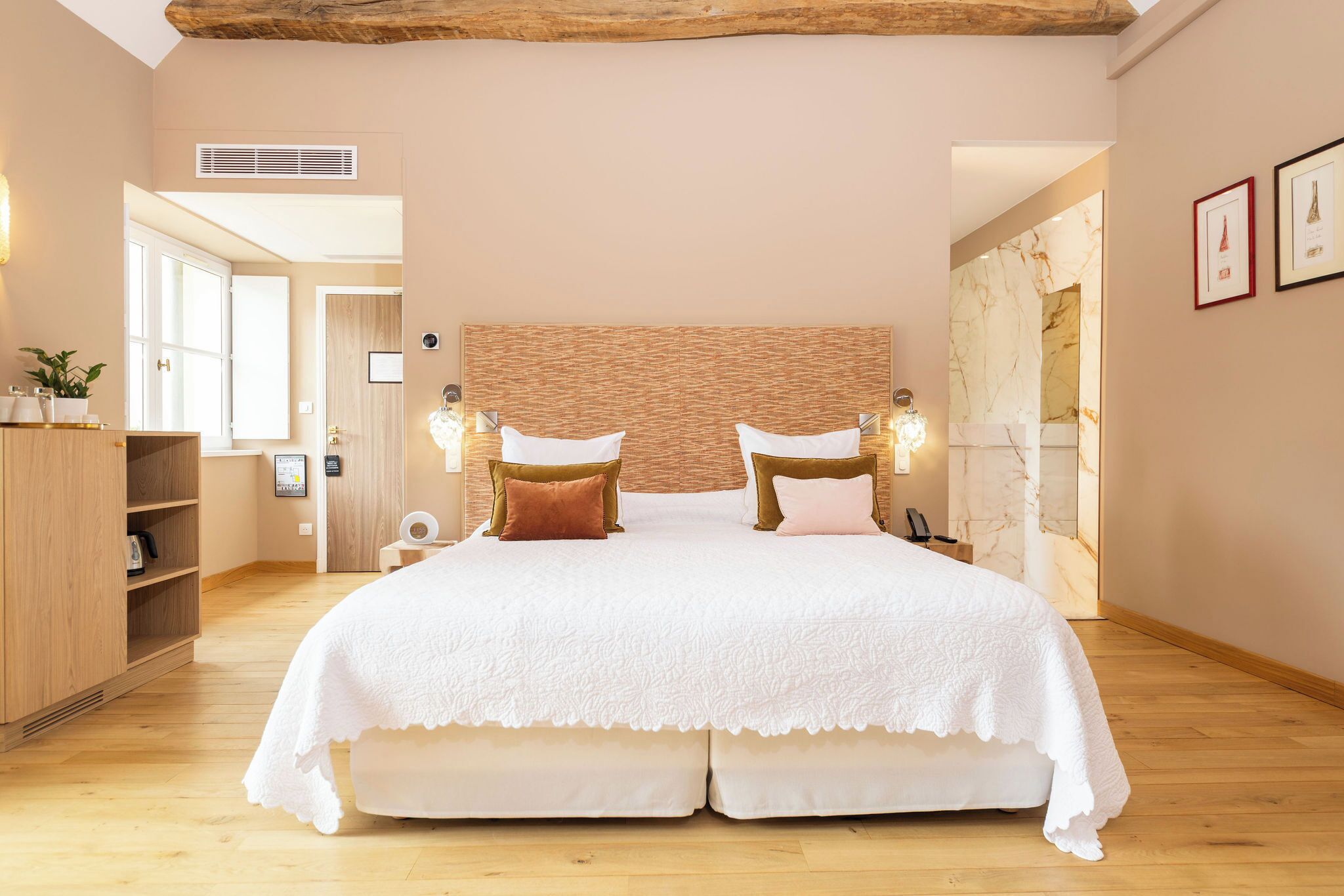 A bedroom with a large bed, wooden headboard, bedside lamps, a wooden wardrobe, and a marble wall.