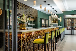 Uma área de bar com design moderno, com balcão, assentos com cadeiras amarelas e plantas decorativas.