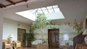 A spacious room with a high ceiling, a skylight, and a mural of a landscape. There are wicker chairs, a sofa, and a coffee table. - Alte Hotel (Loulé)