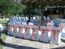 Rows of white chairs with orange sashes, arranged outdoors under a wooden pergola.