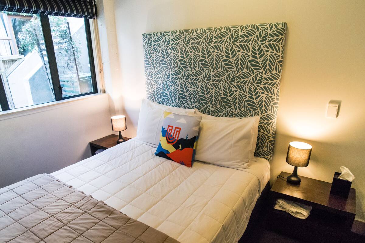 A neatly made bed with a quilted cover, a patterned headboard, and two bedside lamps.