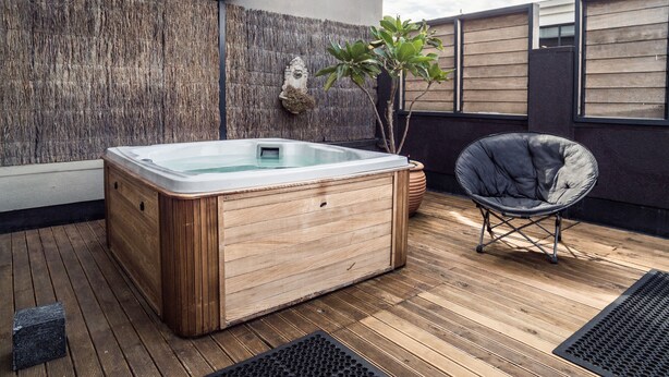 A wooden hot tub on a wooden deck with a chair and a plant.